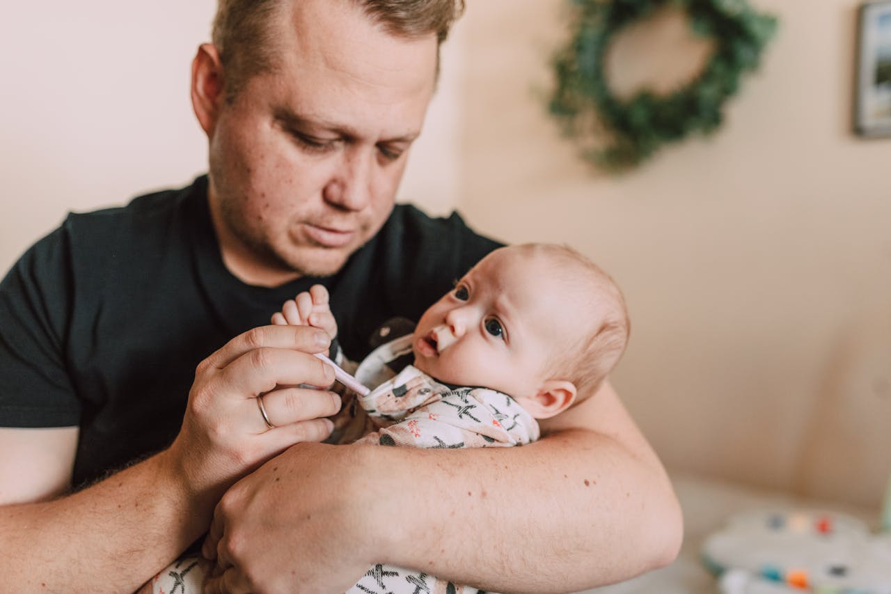 about-us A father tenderly checks his baby’s temperature with a thermometer at home.